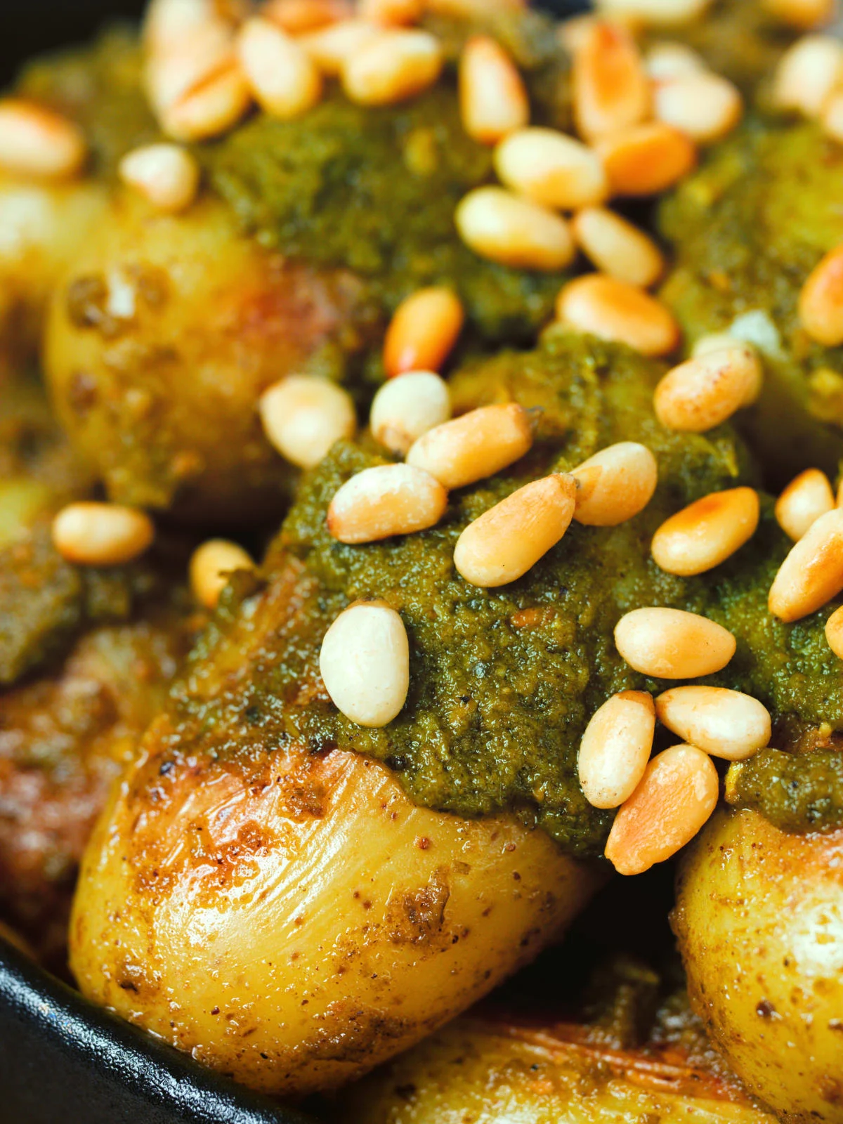 Close-up brown butter and basil pesto potatoes garnished with pine nuts.