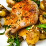 Close-up roasted chicken legs with lemon and thyme served with pesto potatoes and broccoli.