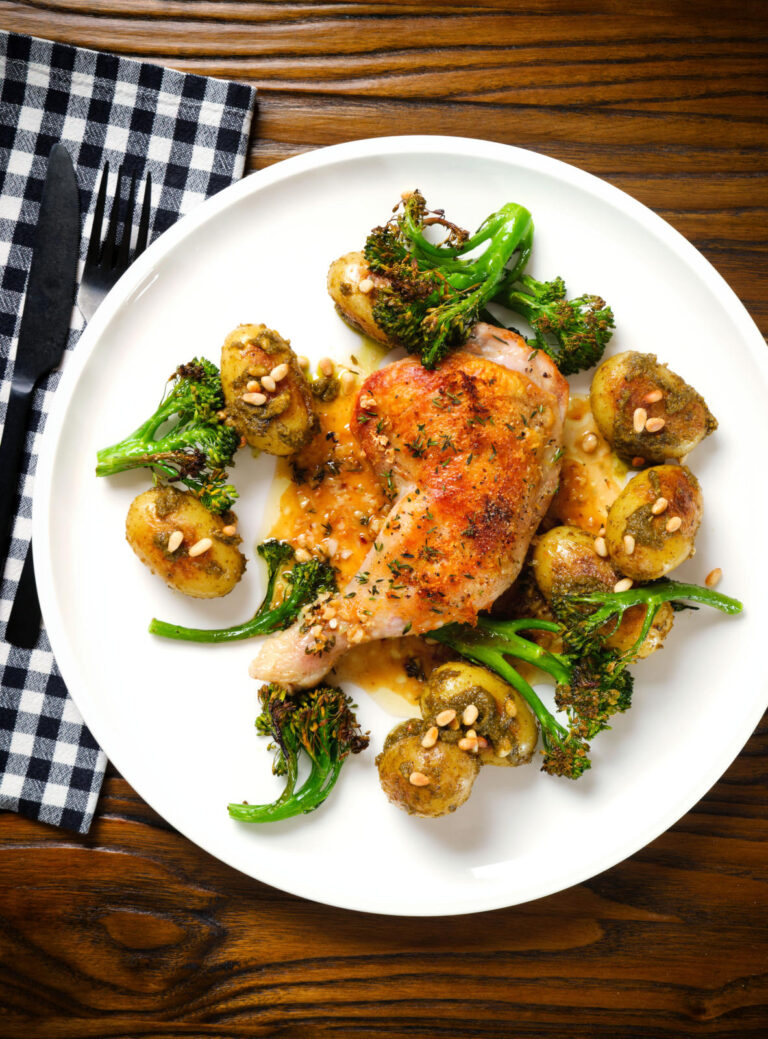 Overhead roasted chicken legs with lemon and thyme served with pesto potatoes and broccoli.
