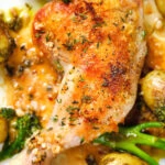 Close-up overhead roasted chicken legs with lemon and thyme served with pesto potatoes and broccoli.