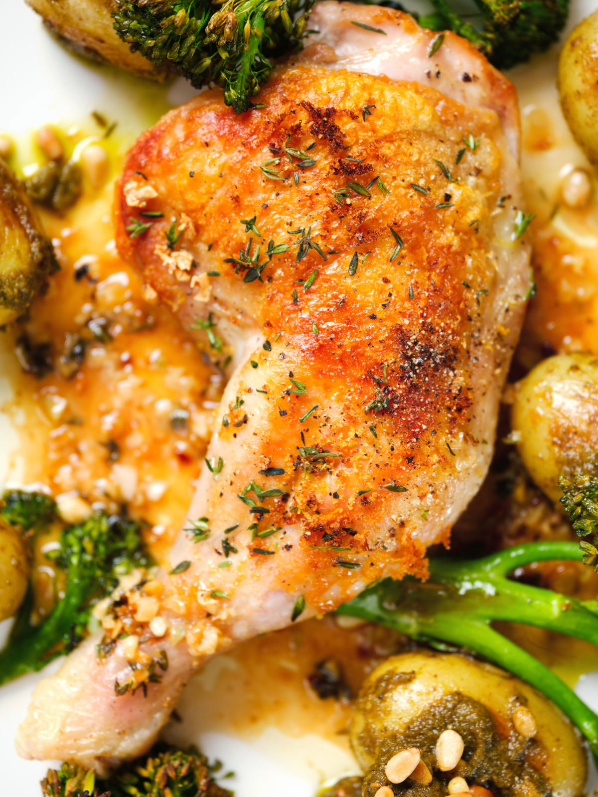 Close-up overhead roasted chicken legs with lemon and thyme served with pesto potatoes and broccoli.
