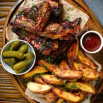 Overhead sticky BBQ sauce glazed lamb spare ribs served with potato wedges and pickles.