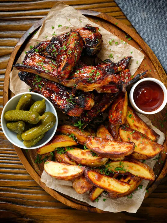 Overhead sticky BBQ sauce glazed lamb spare ribs served with potato wedges and pickles.