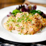Cheesy chicken, bacon and potato gratin on a plate with a side salad.