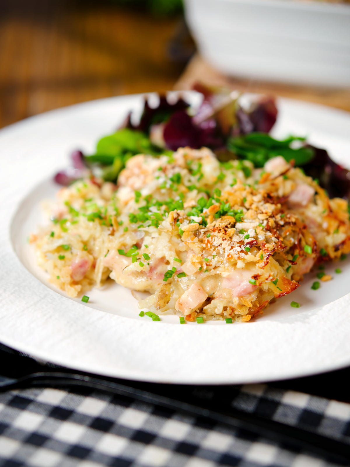 Cheesy chicken, bacon and potato gratin on a plate with a side salad.