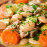 Close-up chicken and butterbean stew with leeks and carrots served with bread.