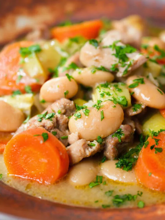 Close-up chicken and butterbean stew with leeks and carrots served with bread.