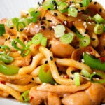 Close-up garlic chicken udon noodles stir fry with crispy chilli oil.