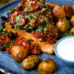 Close-up curried pork chops with tomatoes and raisins served with aloo jeera and raita.
