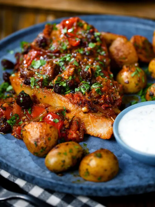 Close-up curried pork chops with tomatoes and raisins served with aloo jeera and raita.
