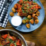 Overhead curried pork chops with tomatoes and raisins served with aloo jeera and raita.