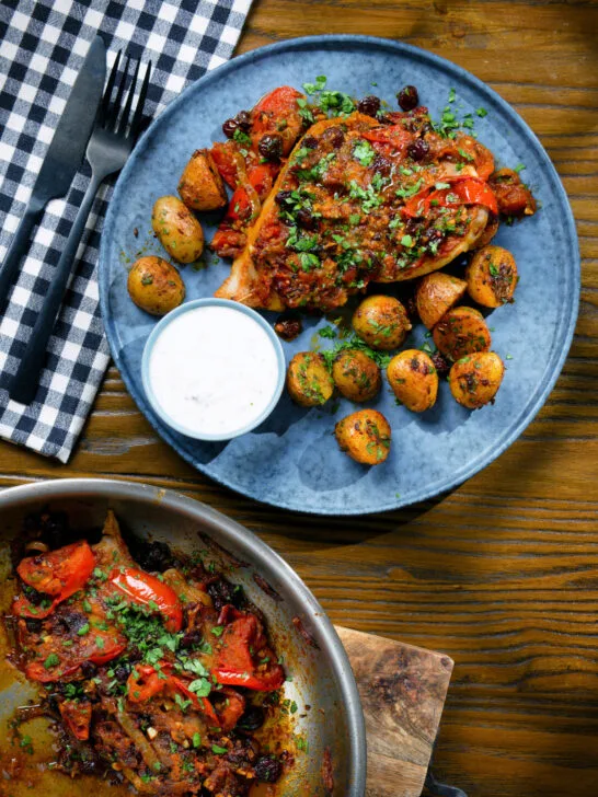Overhead curried pork chops with tomatoes and raisins served with aloo jeera and raita.