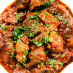 Close-up overhead Filipino beef mechado stew with carrots and potatoes in a tomato sauce.