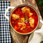 Overhead Filipino chicken afritada stew with potatoes, carrots, peppers and peas in its cooking pot.