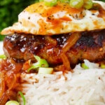 Close-up Hawaiian loco moco: beef patty, white rice, gravy and a fried egg.
