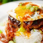 Close-up Hawaiian loco moco: beef patty, white rice, gravy and a fried egg with a runny yolk.