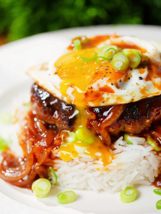 Close-up Hawaiian loco moco: beef patty, white rice, gravy and a fried egg with a runny yolk.