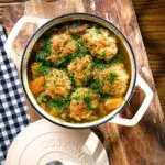 Overhead minted lamb stew with dumplings, swede and carrots in a cooking pot.