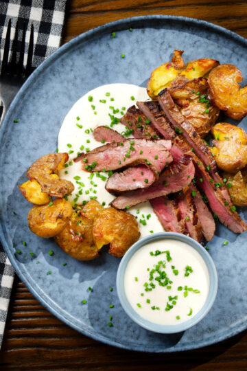 Overhead French soubise (onion sauce) with bavette steak and crushed roasted potatoes.
