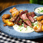 Marinated steak bavette (Flank Steak) served with soubise sauce and crushed roasted new potatoes.