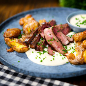 Marinated steak bavette (Flank Steak) served with soubise sauce and crushed roasted new potatoes.