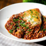 Chicken leg and pearl barley stew with red wine and prunes garnished with parsley..