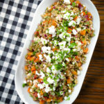 Overhead warm freekeh salad with feta cheese, peppers, tomatoes and parsley.