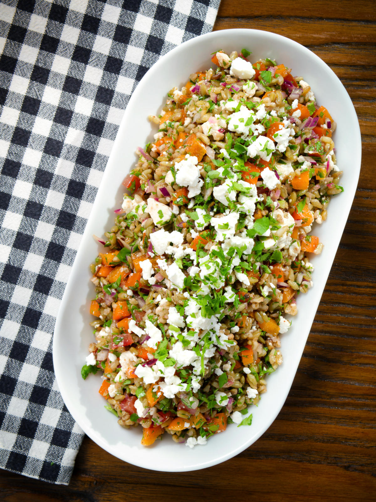 Overhead warm freekeh salad with feta cheese, peppers, tomatoes and parsley.