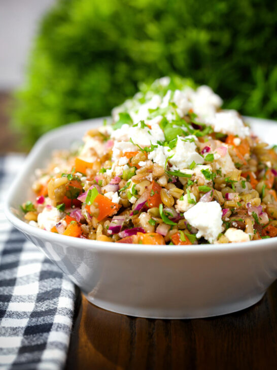 Close-up warm freekeh salad with feta cheese, peppers, tomatoes and parsley.