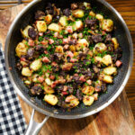 Overhead ham, black pudding and potato hash with snipped chives in a cooking pan.