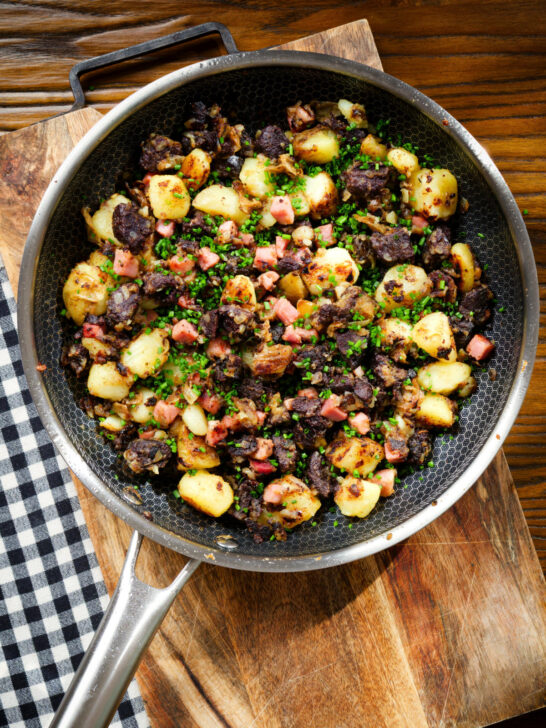 Overhead ham, black pudding and potato hash with snipped chives in a cooking pan.