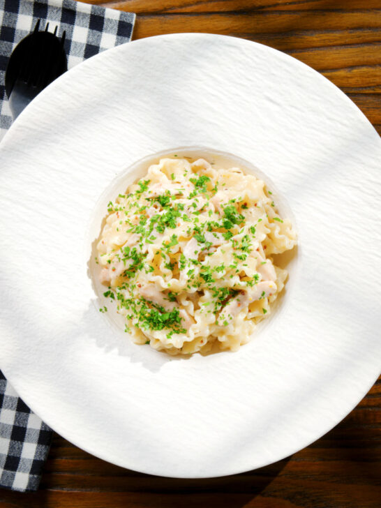 Overhead honey and mustard chicken pasta (malfadine) with chopped parsley.