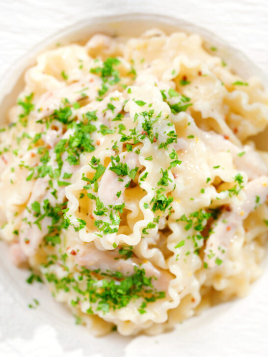Overhead close-up honey and mustard chicken pasta (malfadine) with chopped parsley.