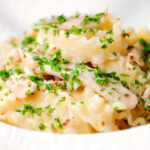 Close-up honey and mustard chicken pasta (malfadine) with chopped parsley.