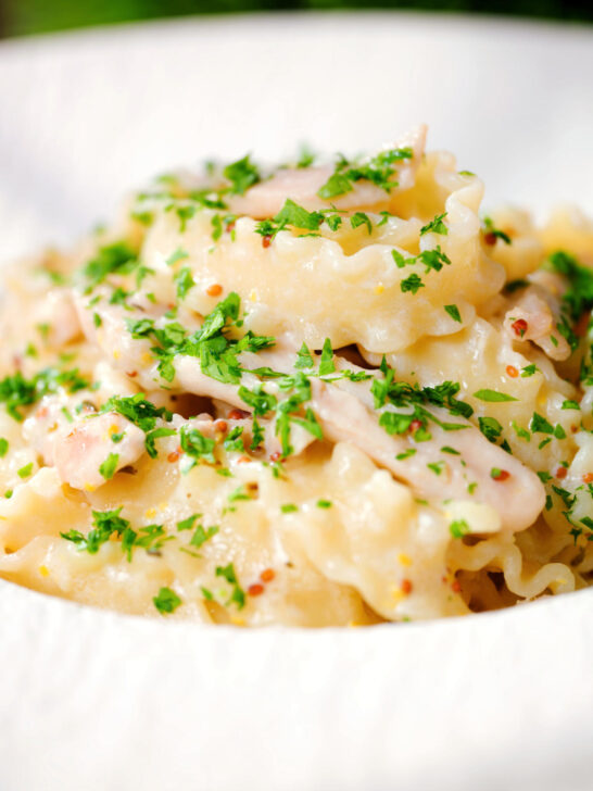 Close-up honey and mustard chicken pasta (malfadine) with chopped parsley.