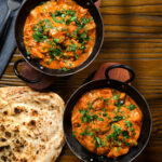 Overhead Kashmiri-style chicken curry served in a kadai with coriander and a naan bread.