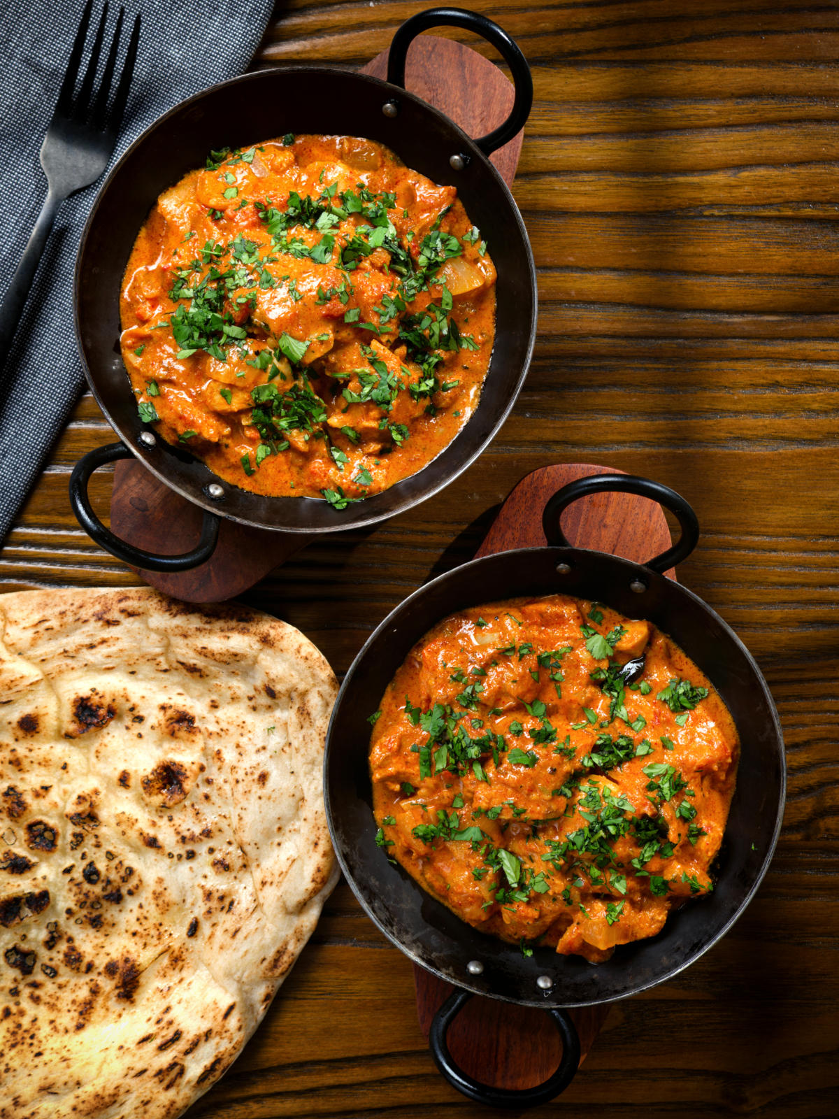 Overhead Kashmiri-style chicken curry served in a kadai with coriander and a naan bread.