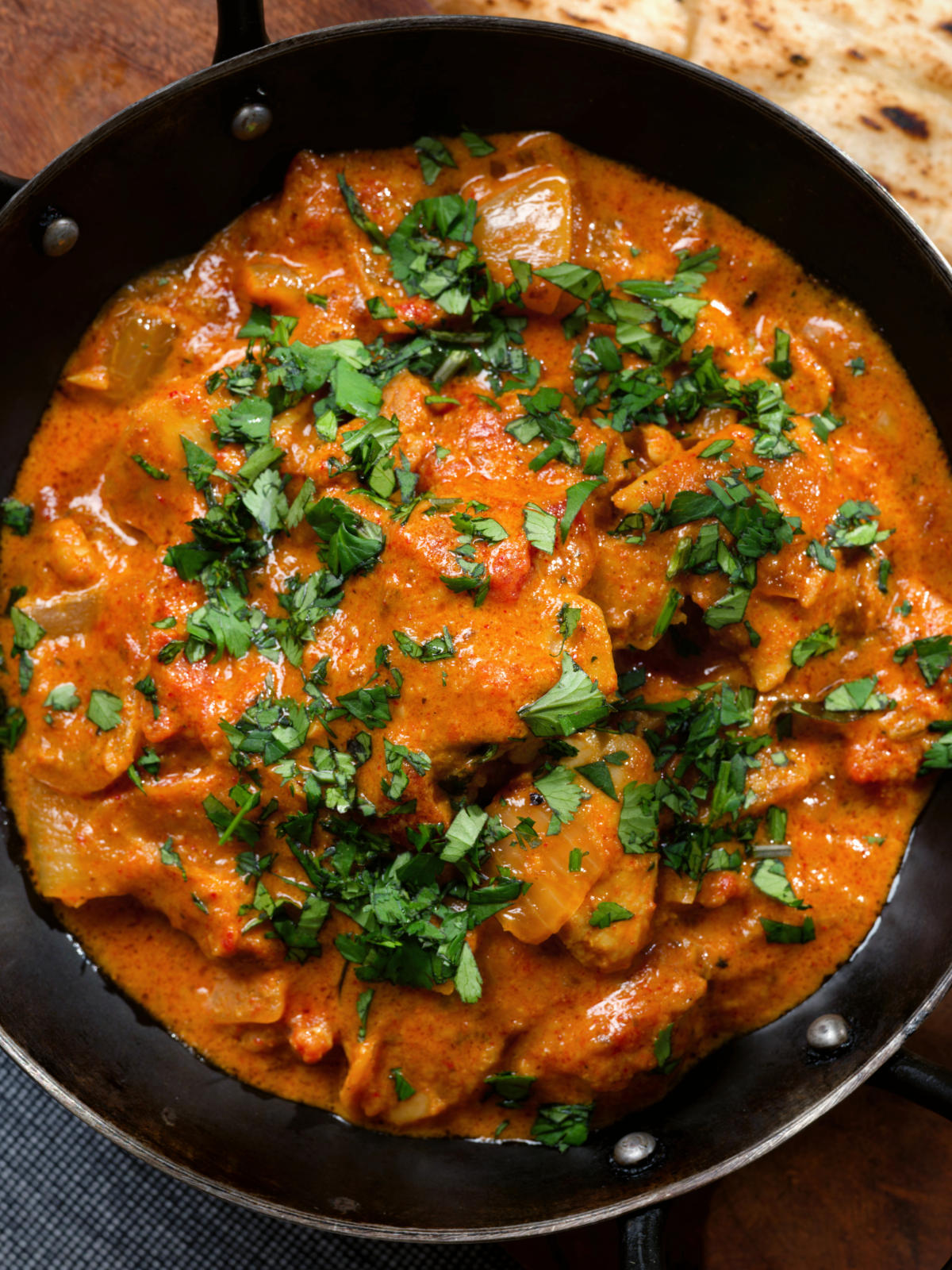 Overhead close-up Kashmiri-style chicken curry served in a kadai with coriander.