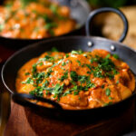 Kashmiri-style chicken curry served in a kadai with coriander and a naan bread.