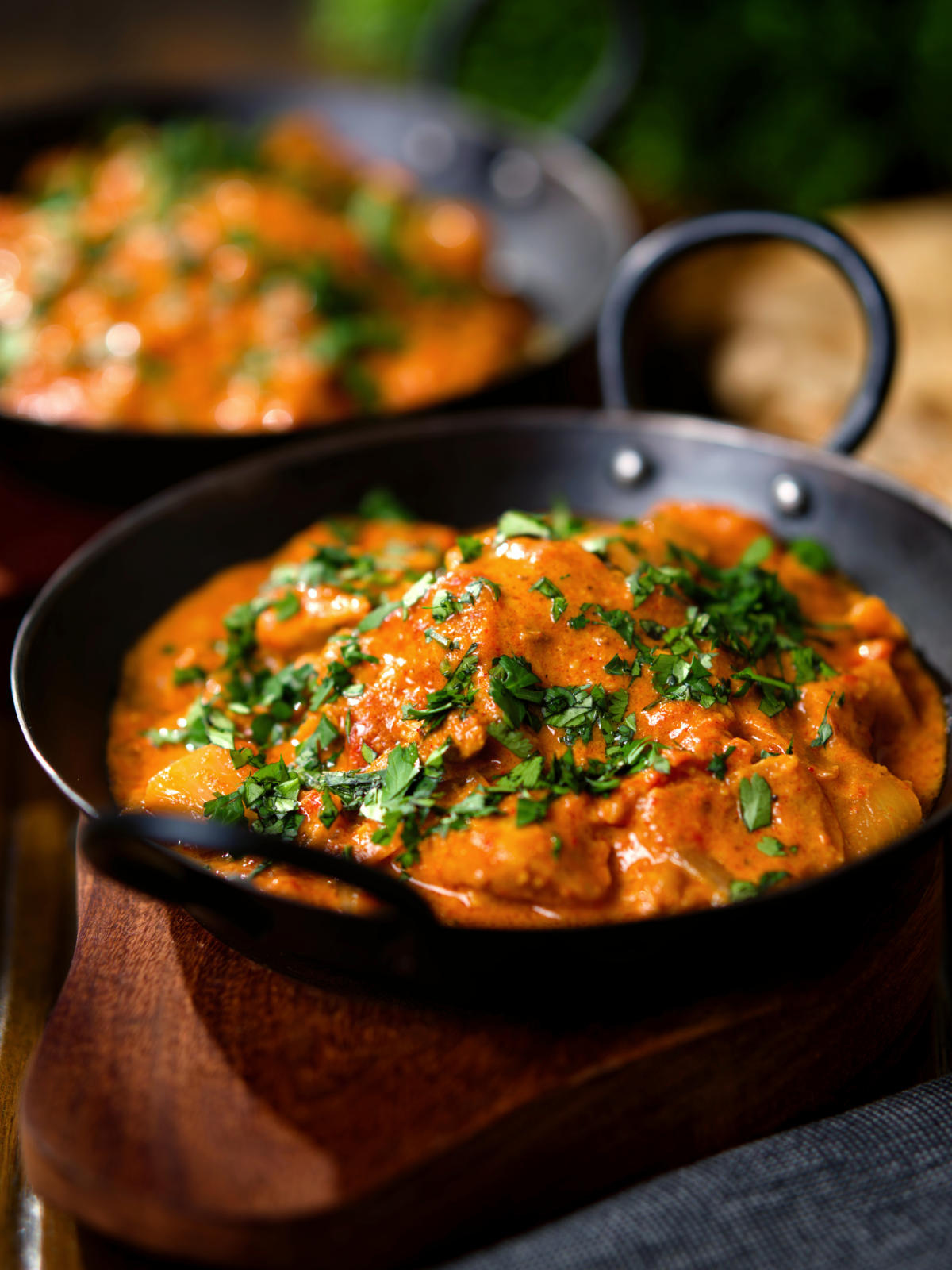 Kashmiri-style chicken curry served in a kadai with coriander and a naan bread.