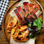 Overhead Korean gochujang glazed pork ribs served with potato wedges.