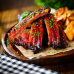 Korean gochujang pork ribs served with snipped chives and potato wedges.