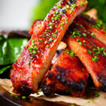 Close-up Korean gochujang glazed pork ribs served with snipped chives.