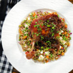 Overhead baked pomegranate molasses duck leg with onions, served with a feta freekeh salad.