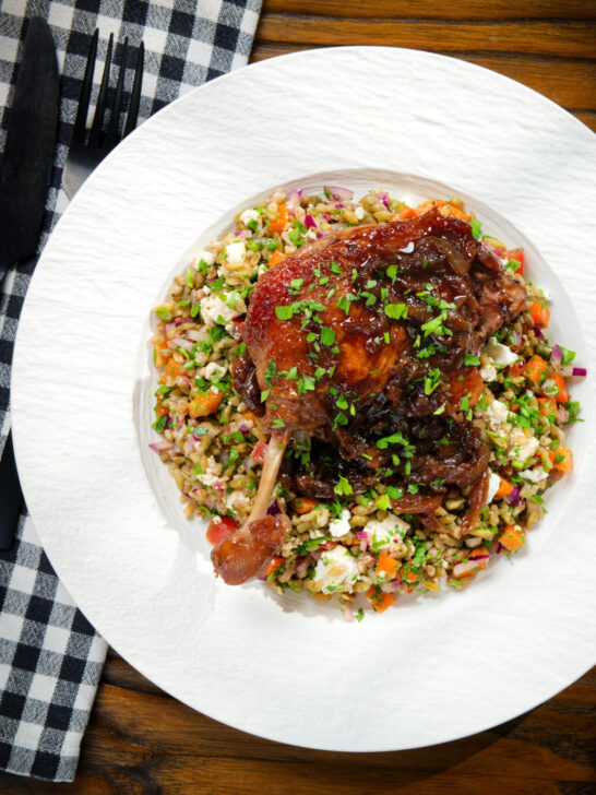 Overhead baked pomegranate molasses duck leg with onions, served with a feta freekeh salad.