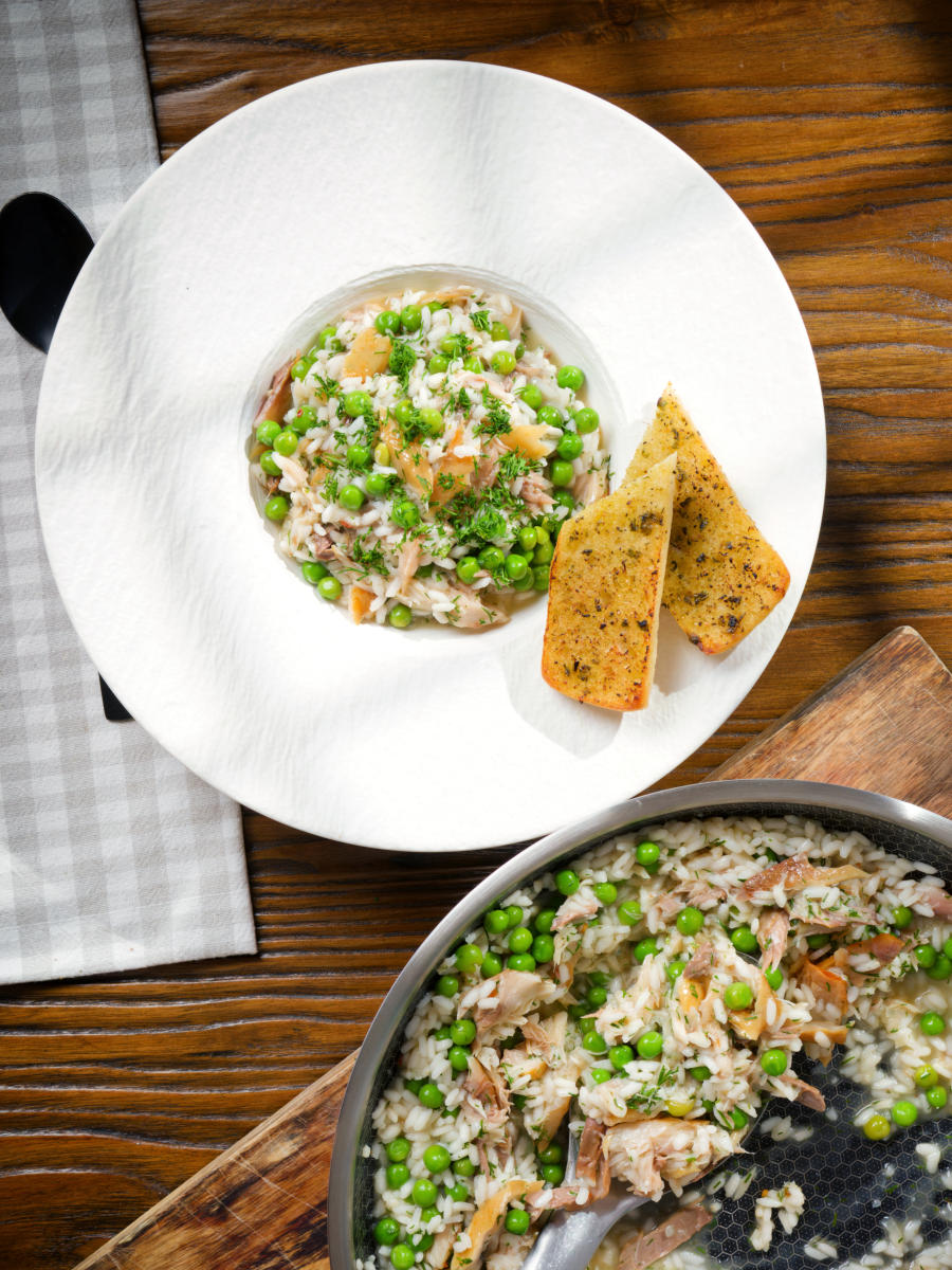 Overhead smoked mackerel risotto with peas and dill served with garlic bread.
