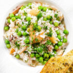 Overhead close-up smoked mackerel risotto with peas and dill served with garlic bread.