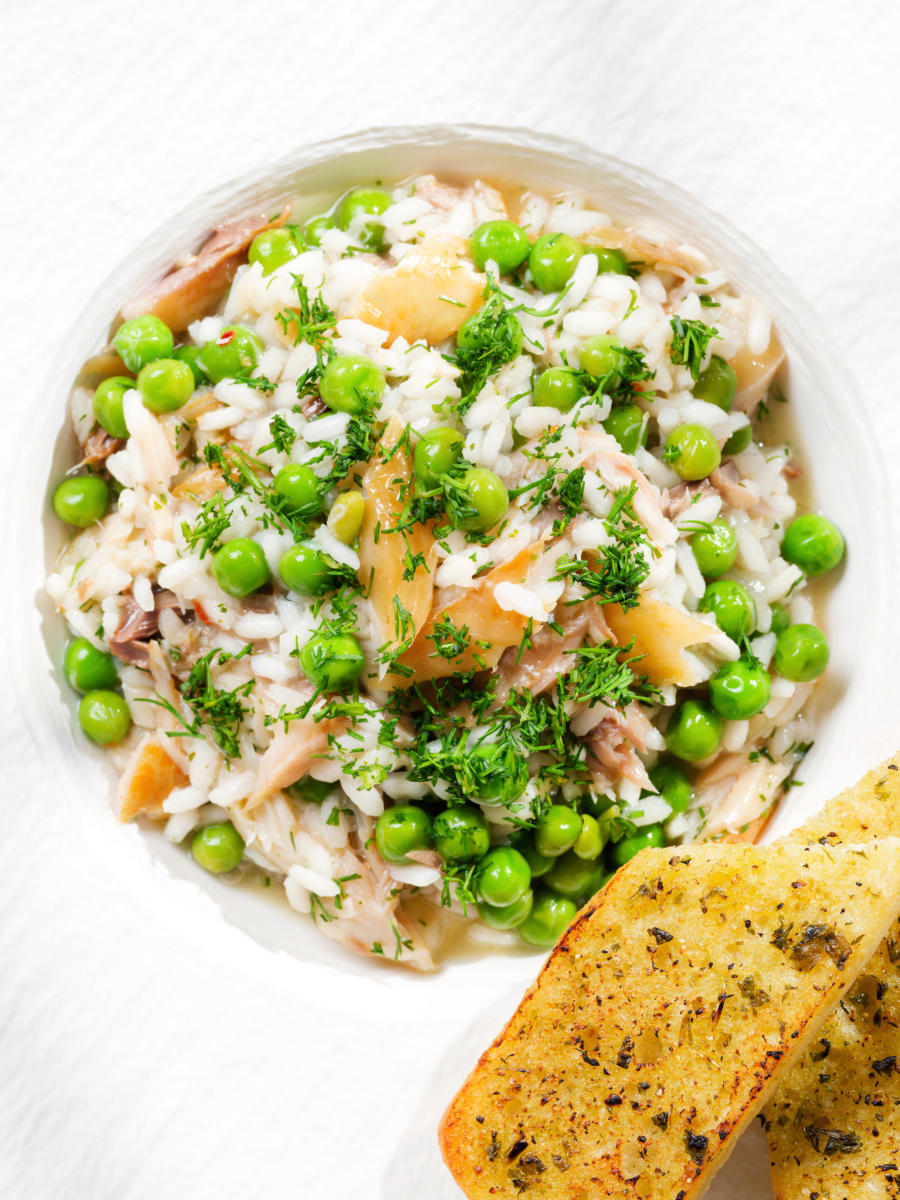 Overhead close-up smoked mackerel risotto with peas and dill served with garlic bread.