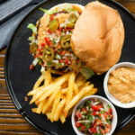 Overhead Mexican beef burger with salsa fresca, chipotle mayonnaise served with French fries.