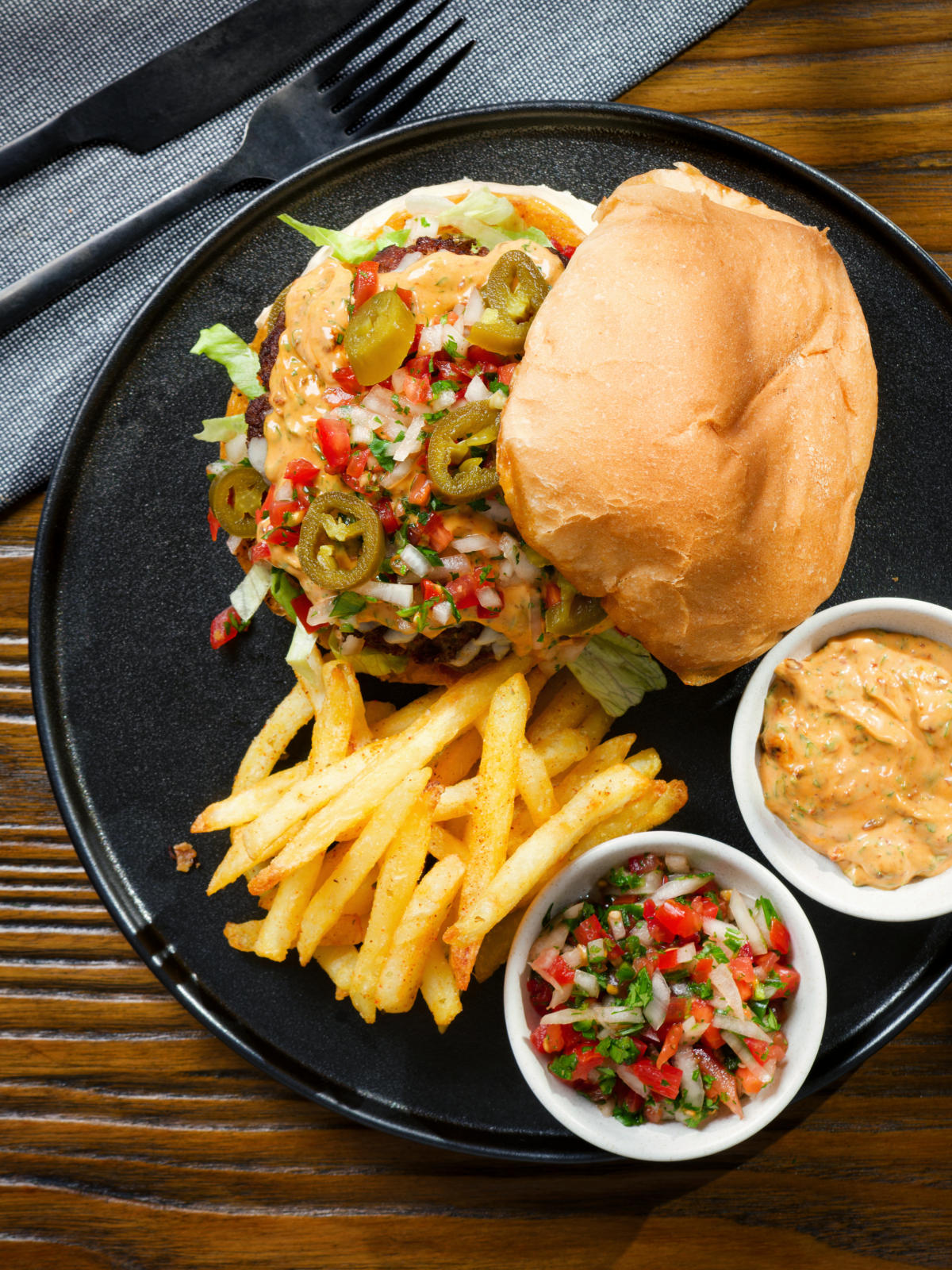 Overhead Mexican beef burger with salsa fresca, chipotle mayonnaise served with French fries.